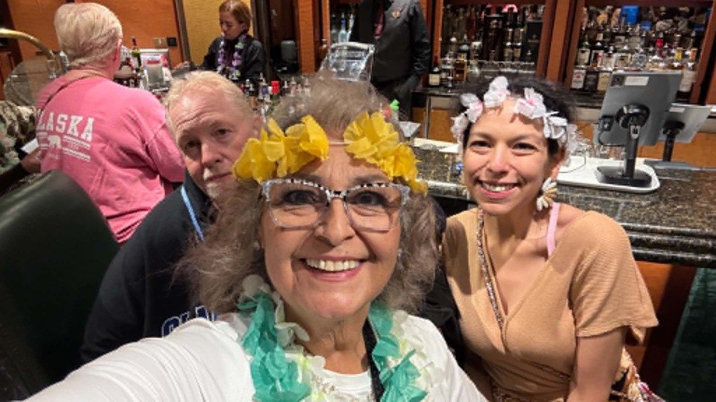 Pat Kahn, Lupe Soto and Angela Garcia pose at the bar wearing Hawaiian leis and headbands during theme night on the Poker Player Cruises Alaska voyage
