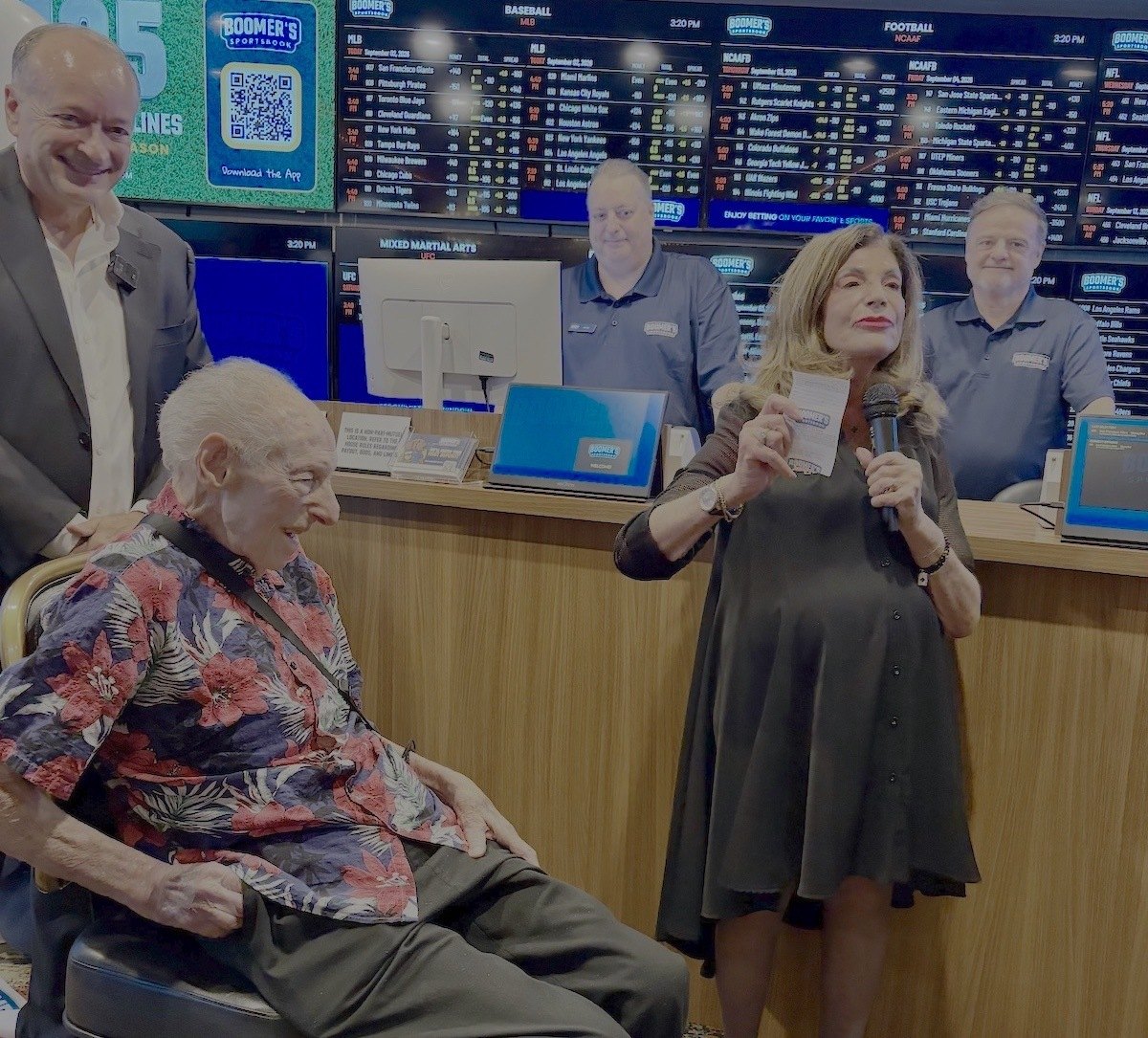 Las Vegas Mayor Shelley Berkley holds up her betting slip while speaking into a microphone as former Mayor Oscar Goodman, seated beside her, looks on at Boomer's Sportsbook inside Four Queens.