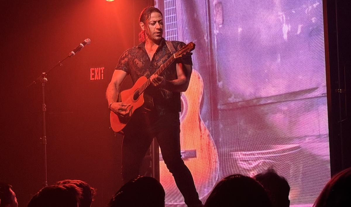 Chippendales dancer Mozart playing an acoustic guitar and singing into a microphone on stage during a live performance in Las Vegas.