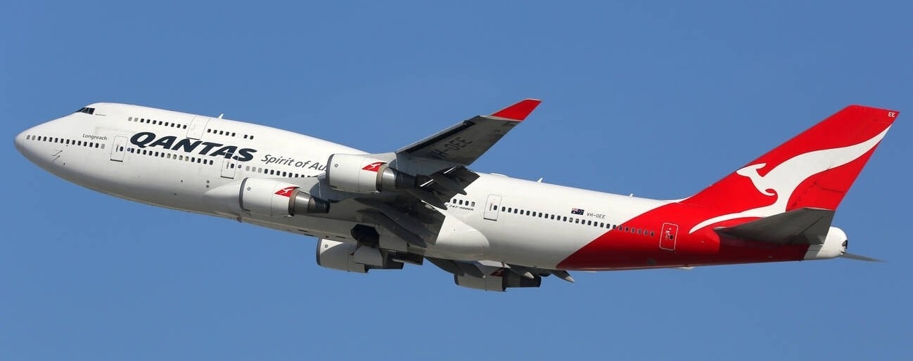 A Qantas plane in flight, showing the red tail and white kangaroo logo on the side of the aircraft