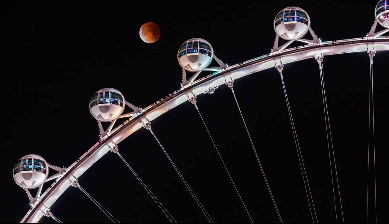 A blood moon lunar eclipse rises behind the High Roller observation wheel on the Las Vegas Strip