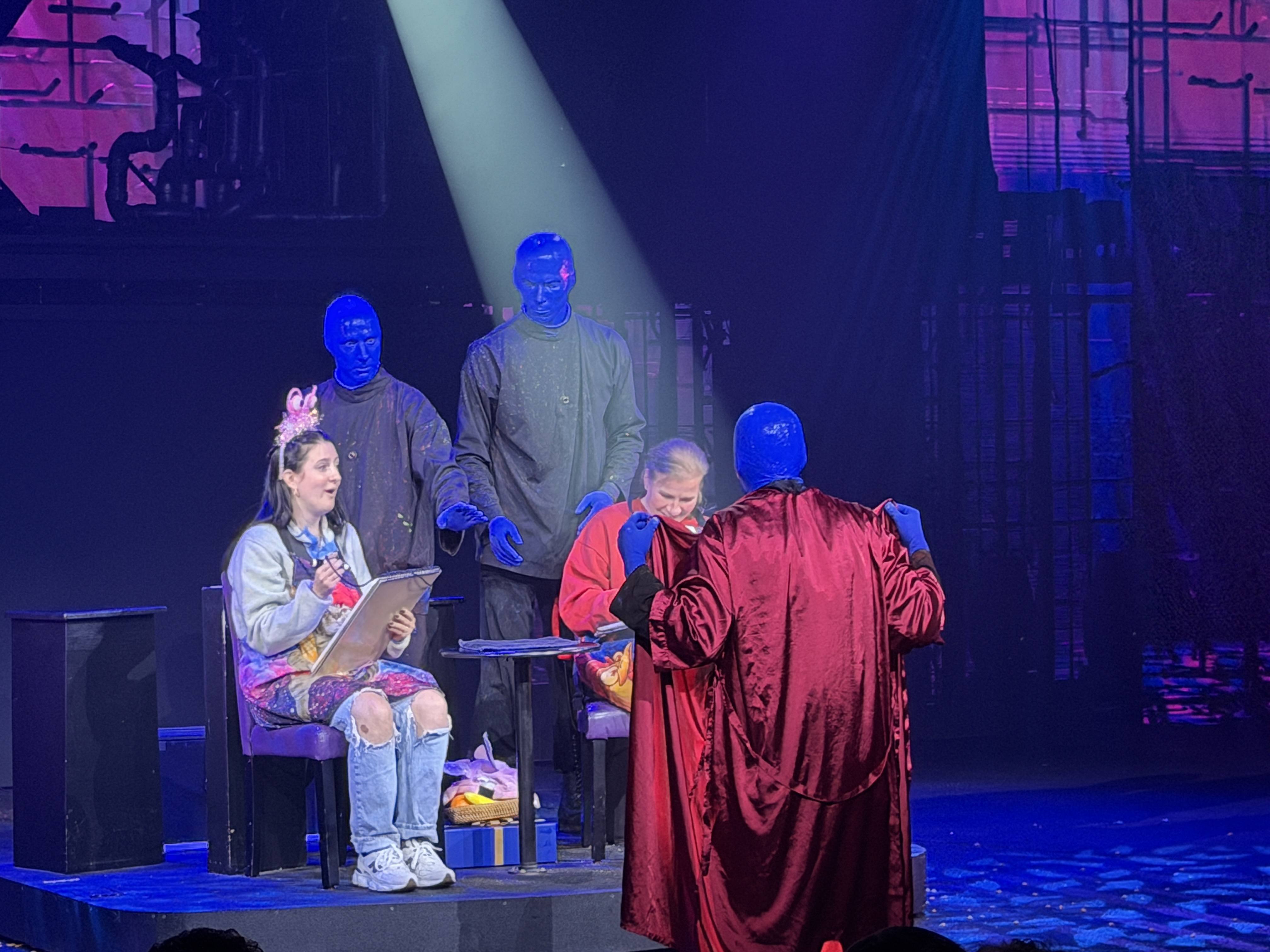 Blue Man Group performers on stage with two audience members