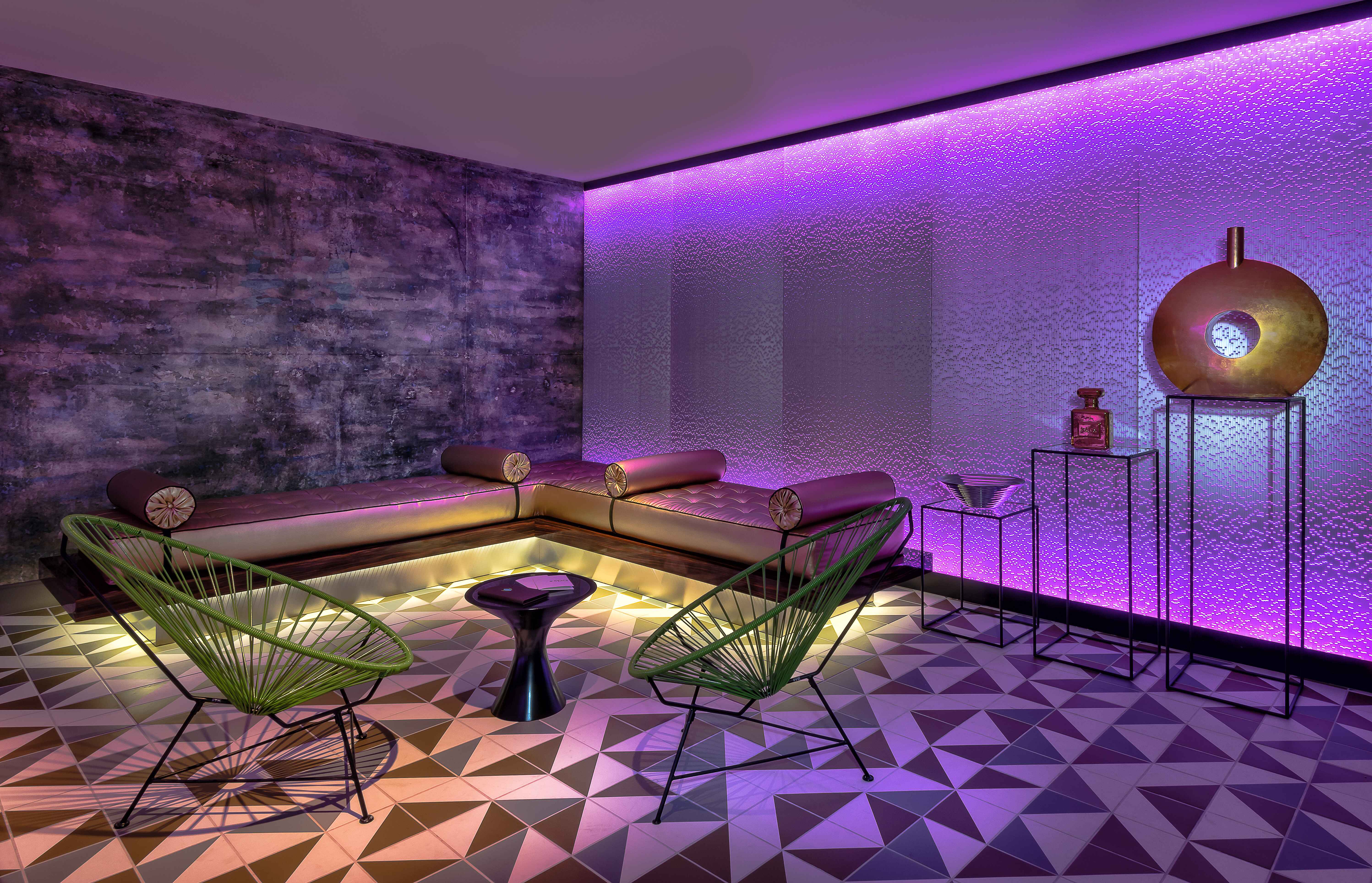 The spa lounge at the LINQ Hotel and Casino with purple LED lights, a couch, and chairs.