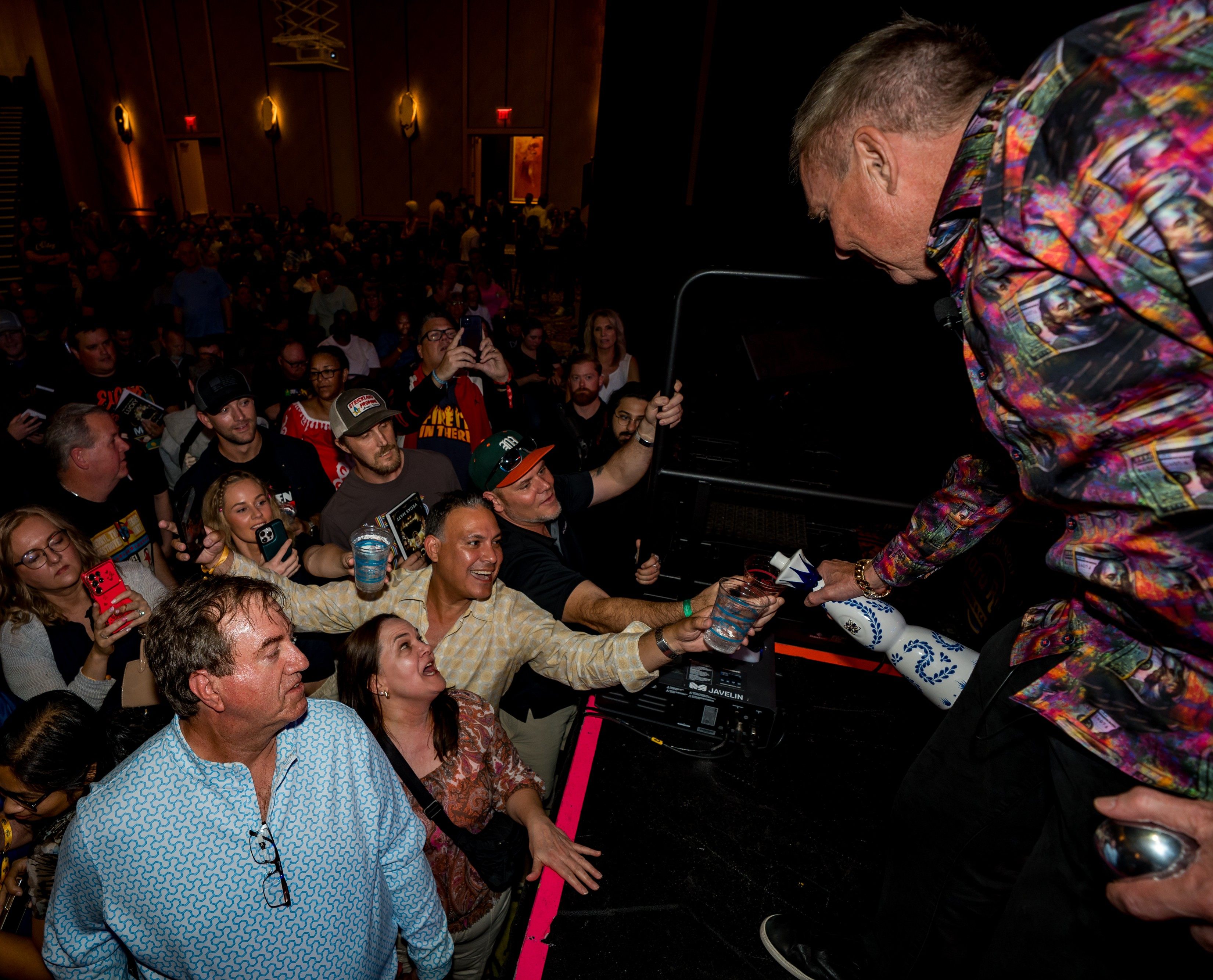 A man pours tequila into the cups of crowd members at an event