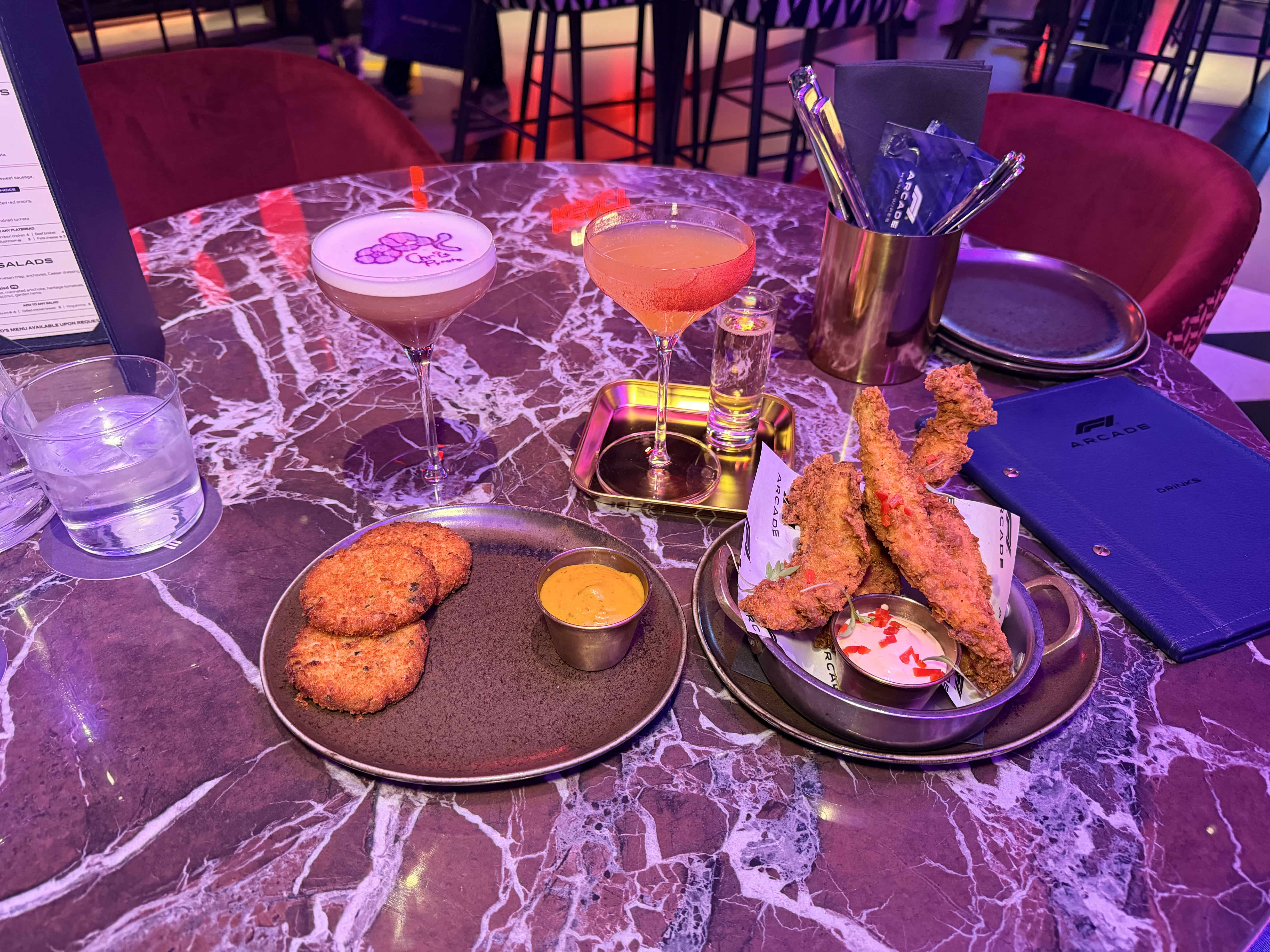 Two cocktails (VIP Pass and Petal Drift) and food at F1 Arcade. Crab fritters and chicken tenders