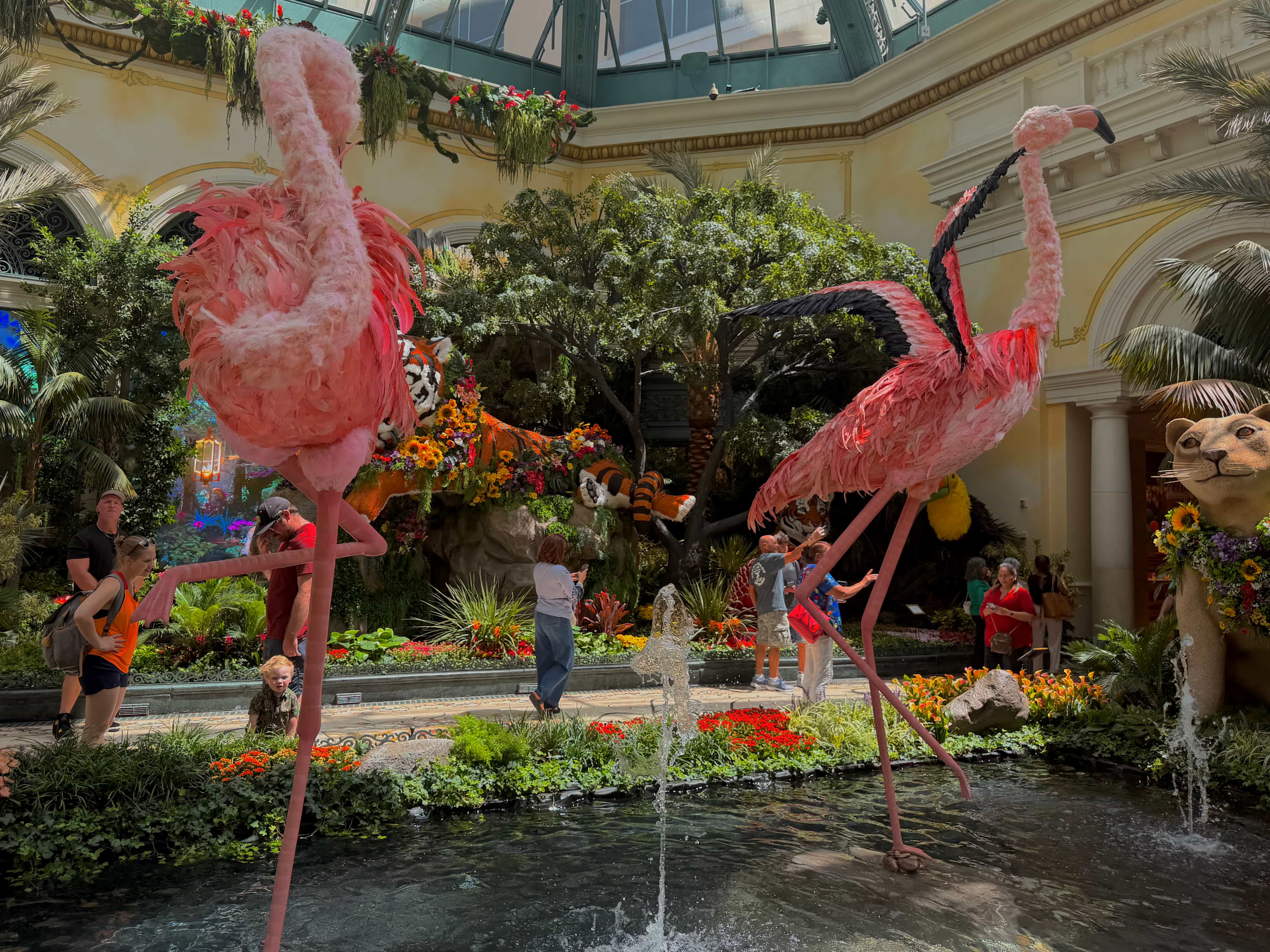 A display of two flamingos on top of a pond with a fountain in the Bellagio Conservatory during the day