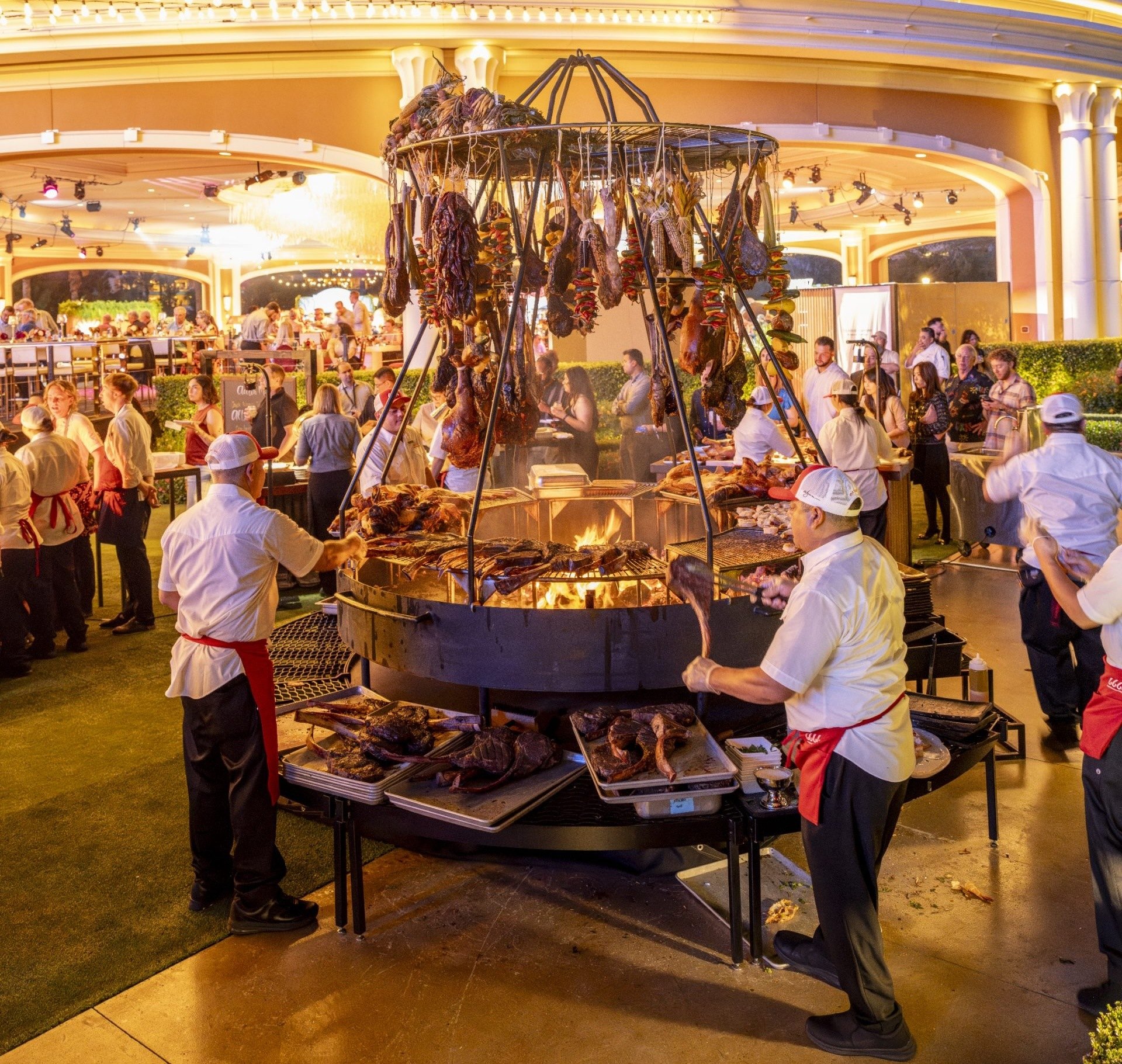 A meat station from Four Sixes (6666) Ranch at Wynn Revelry, with various cuts of meat hanging from a station and several shifts around it.