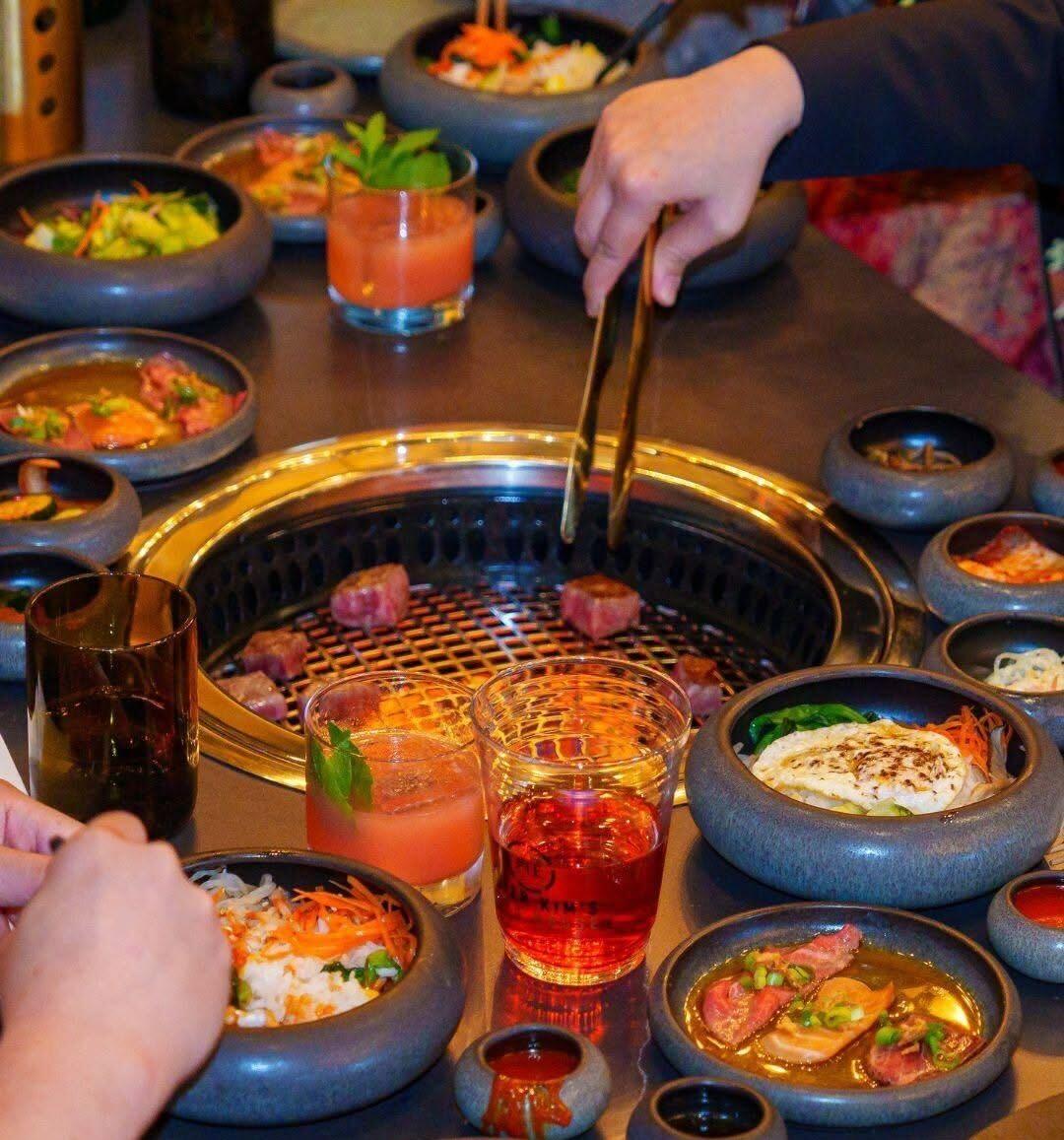 Wagyu beef cooks on a tabletop grill alongside Korean side dishes and cocktails at Master Kim's Wagyu House inside Palace Station.