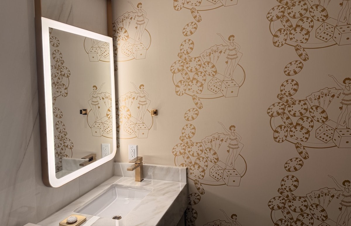 The bathroom inside a new suite at Circa Resort and Casino's rooms on the Platinum Floor. The wallpaper is white with gold accents including a flapper outline, poker chips, dice, and playing cards.