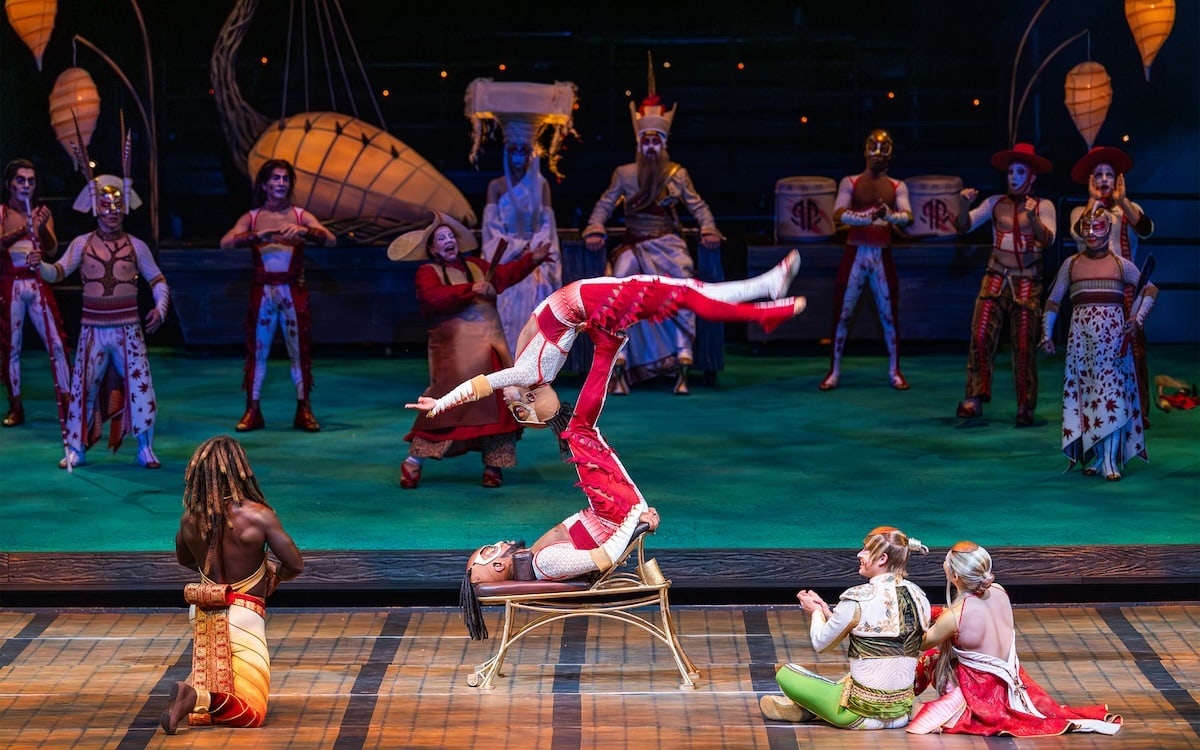 full cast finale on stage with a large creature backdrop and colorful costumes