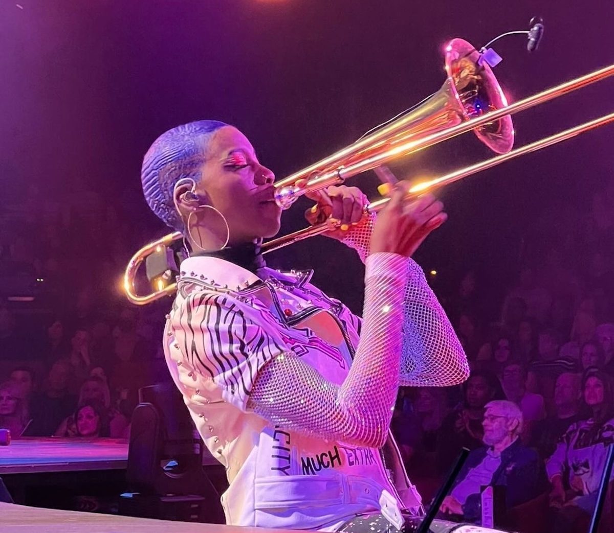 Side profile picture of multi-instrumentalist Tracyan Martin playing the trombone with her eyes closed and a bling jacket during the Mad Apple show at New York New York