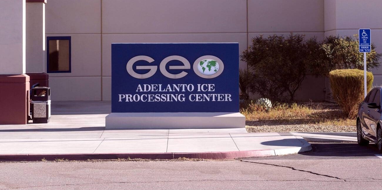 blue sign reads geo adelanto ice processing center outside of a building