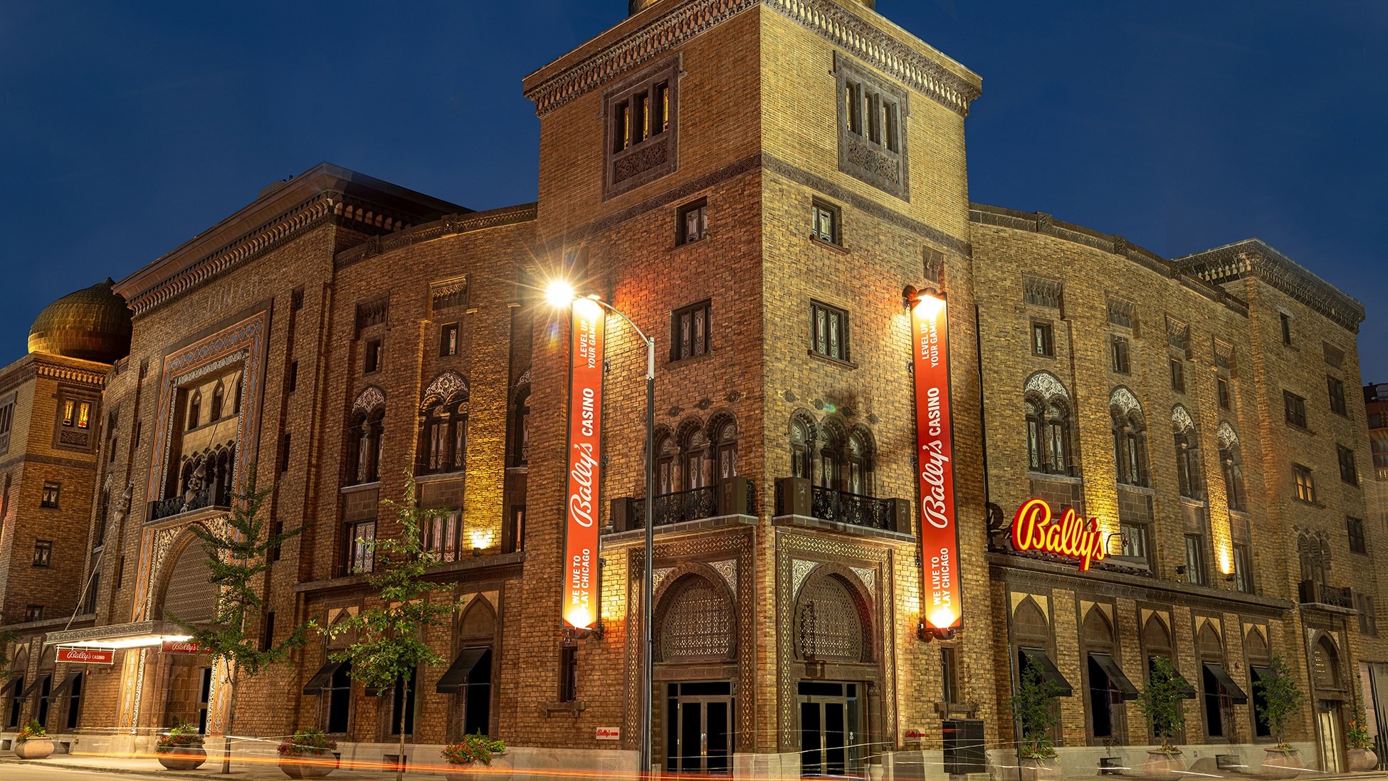 Bally's Casino Chicago illuminated at night, housed in an ornate historic brick building with red banners and neon signage