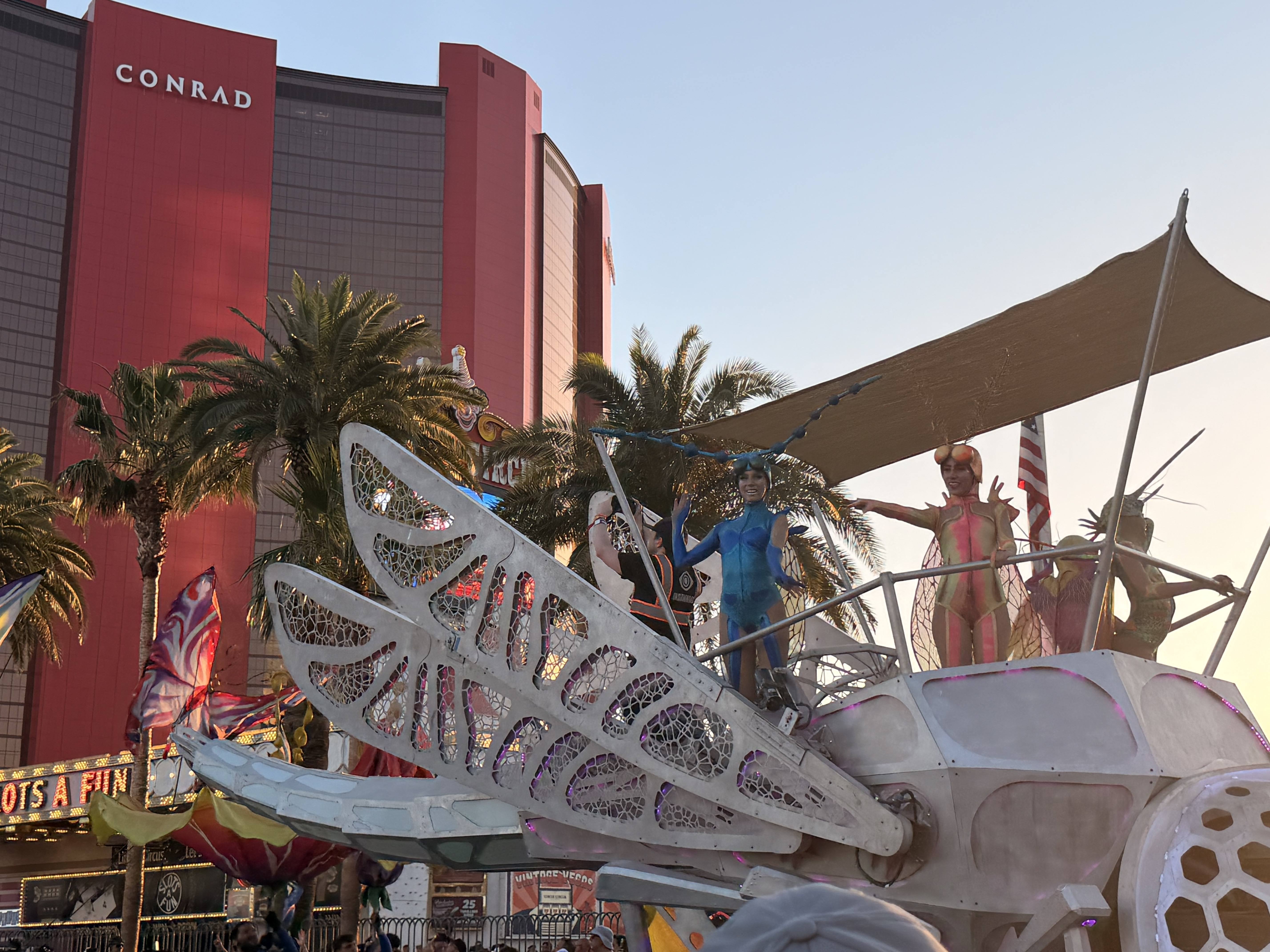 Women stand on a bug themed art car traveling in the EDC World Party Parade in front of Resorts World