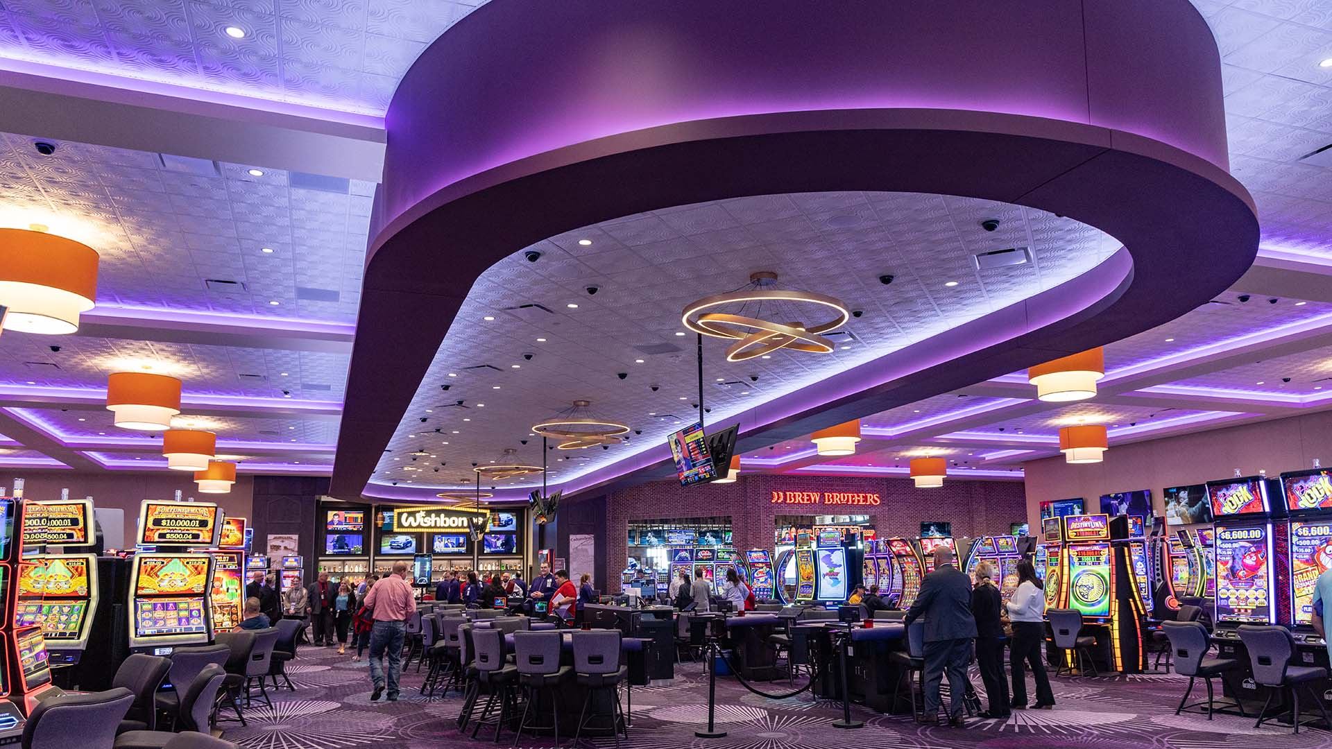 Interior of a modern casino gaming floor with slot machines, poker tables, purple LED lighting, and guests near Brew Brothers bar