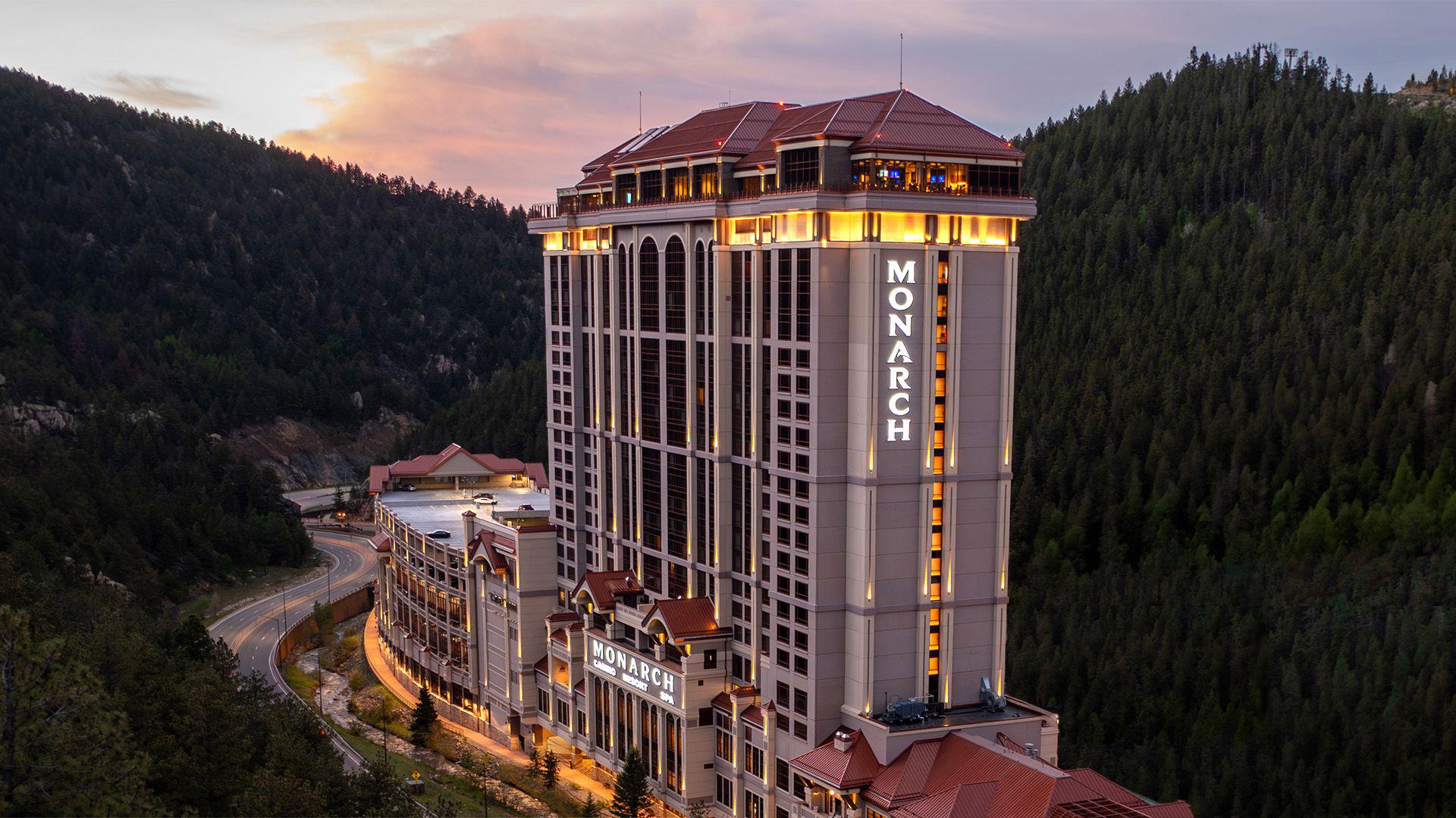 Aerial view of Monarch Casino Resort Spa glowing at dusk nestled between pine-covered mountains in Black Hawk, Colorado